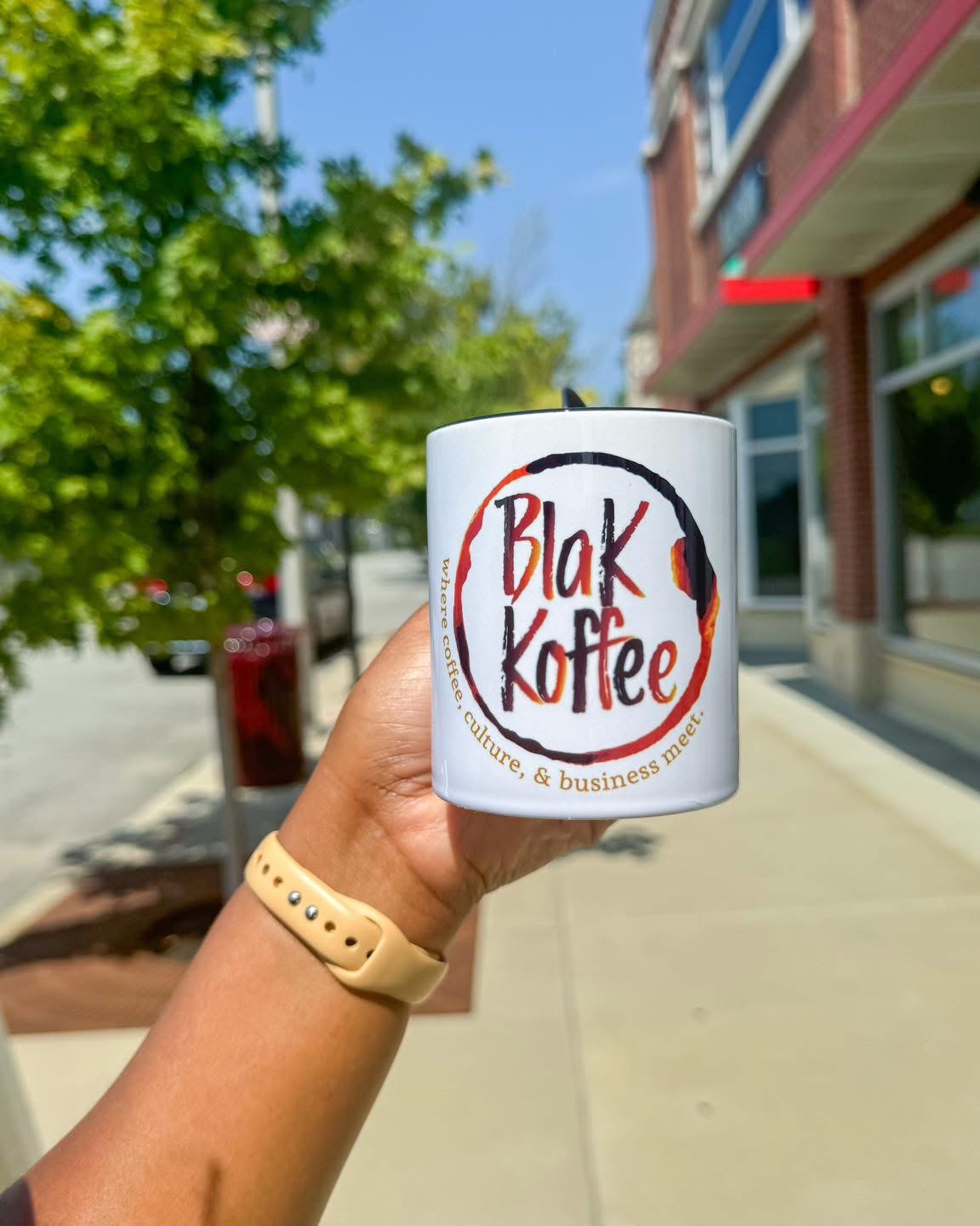 Blak Koffee branded mug held up outside the West End location